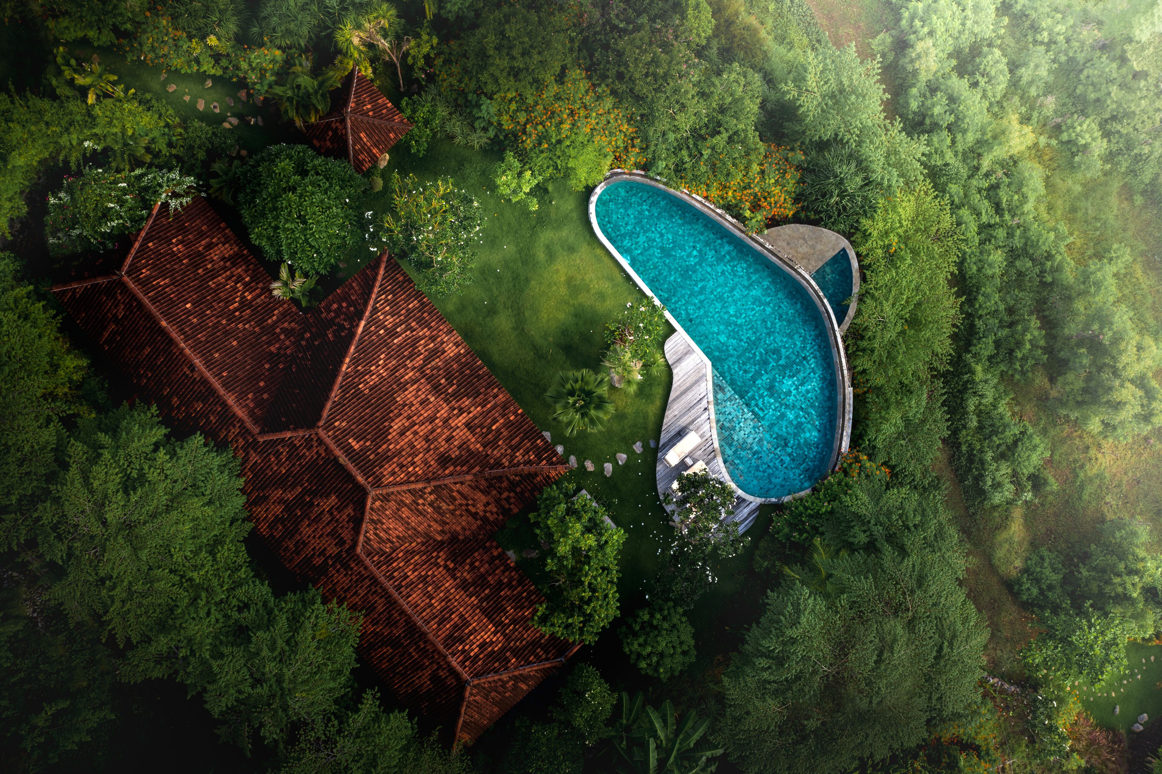An aerial view of a property with a swimming pool surrounded by lush greenery and a hexagonal-roofed building.