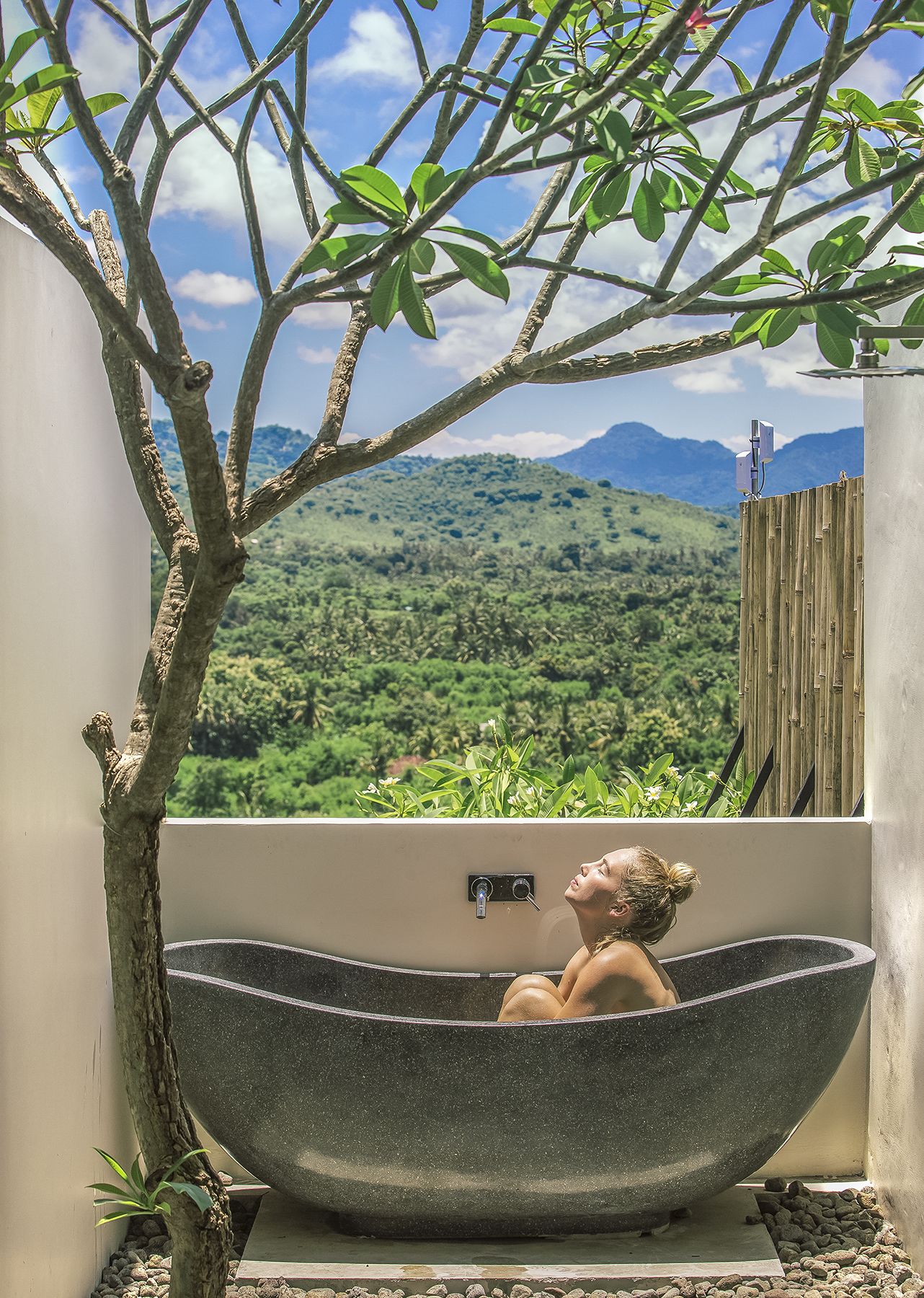 Una bañera en una piedra con vistas a un paisaje verde exuberante y montañas al fondo.