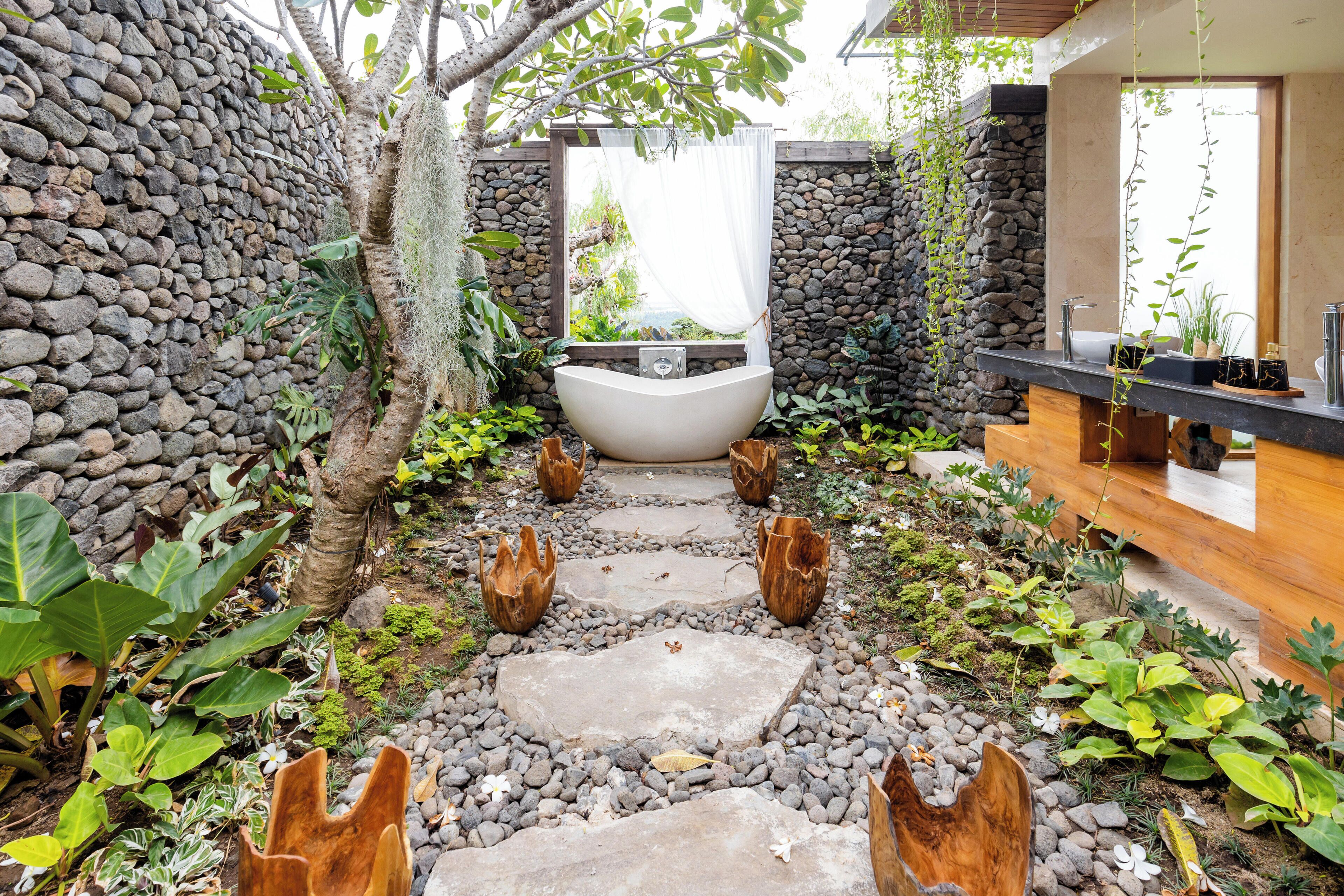 Zona de spa con pared de piedra, una bañera grande y una terraza de madera.
