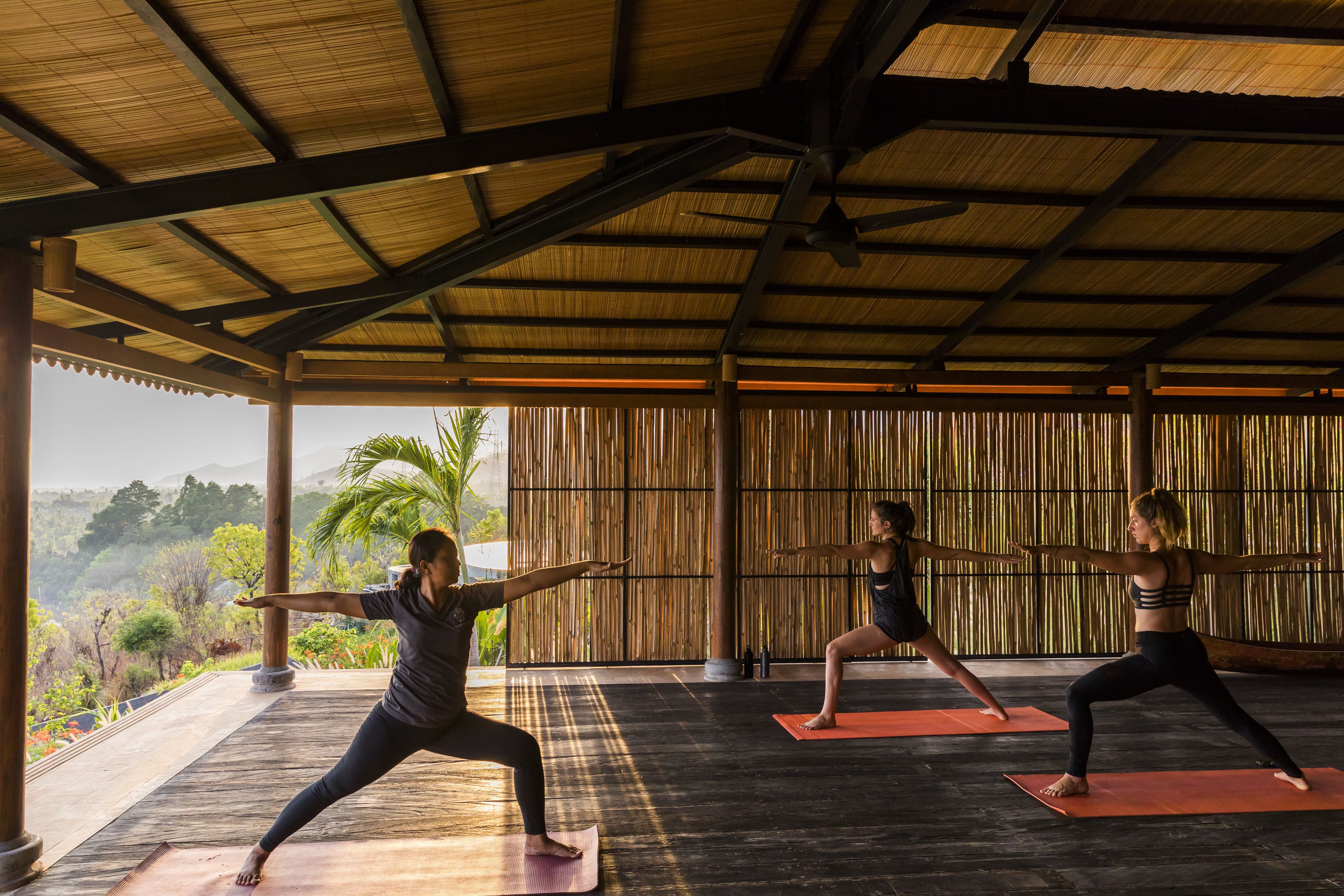 A yoga studio with a view of the outdoors, featuring a wooden ceiling and bamboo walls.
