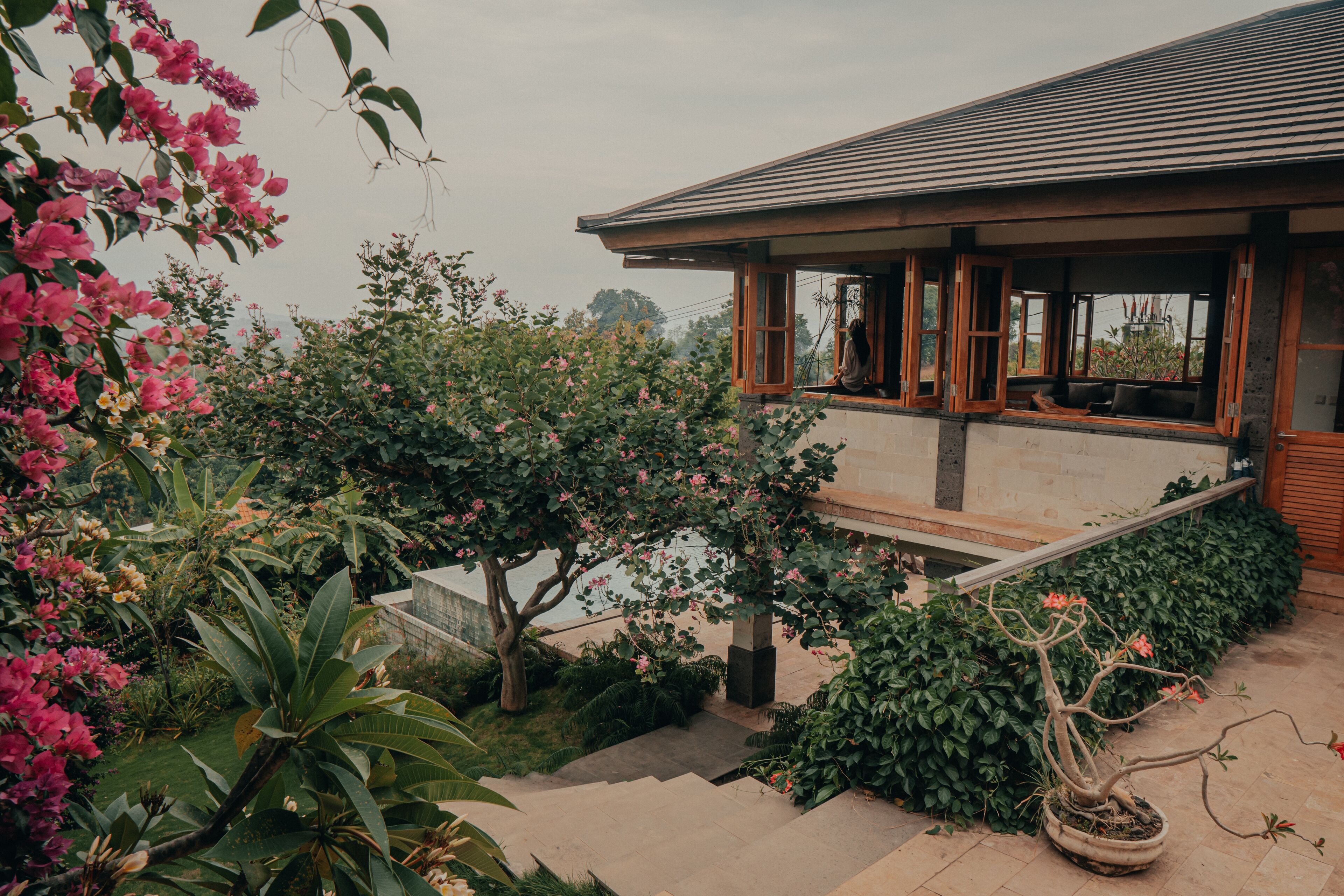 A house with a covered porch, a stone staircase, and lush greenery.