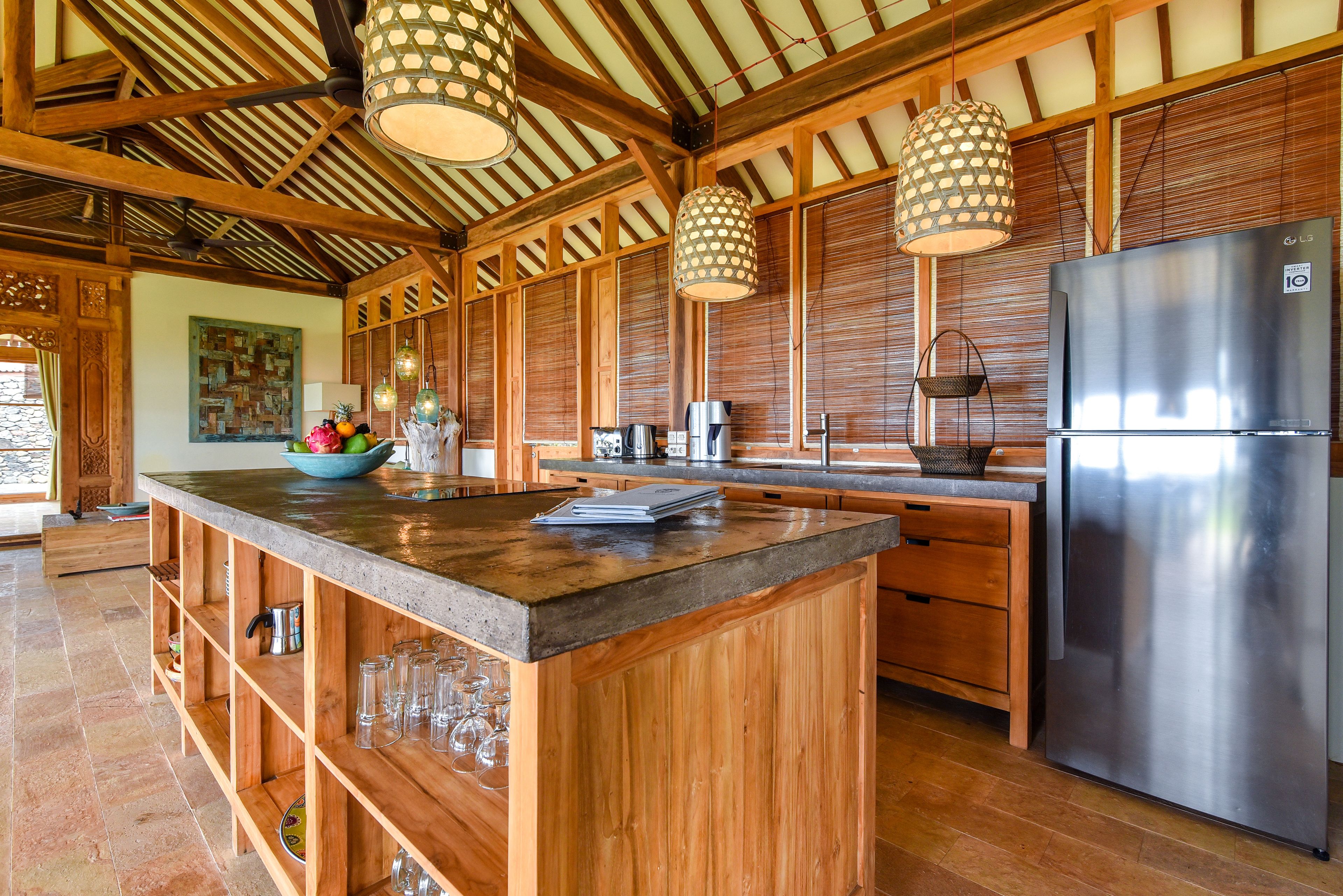 A kitchen with wooden cabinets, a stainless steel refrigerator, and a large island with a bowl of fruit and glasses.