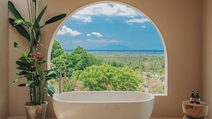 Un baño con un gran ventanal de arco, una bañera y una planta en maceta.