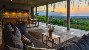 A modern living room with a large sofa, a dining table, and a kitchen area. - Sumberkima Hill Private Villa Retreat (Pemuteran)