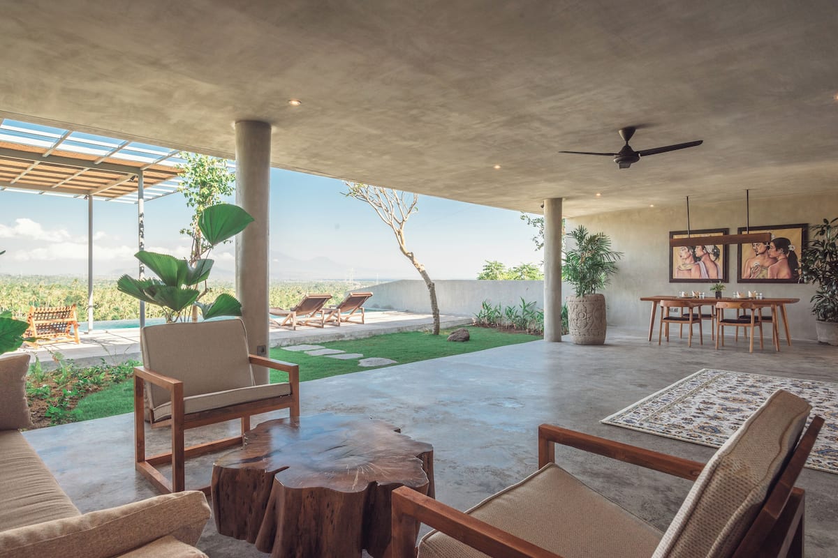 A spacious patio with a concrete floor, wooden furniture, and a view of the landscape.
