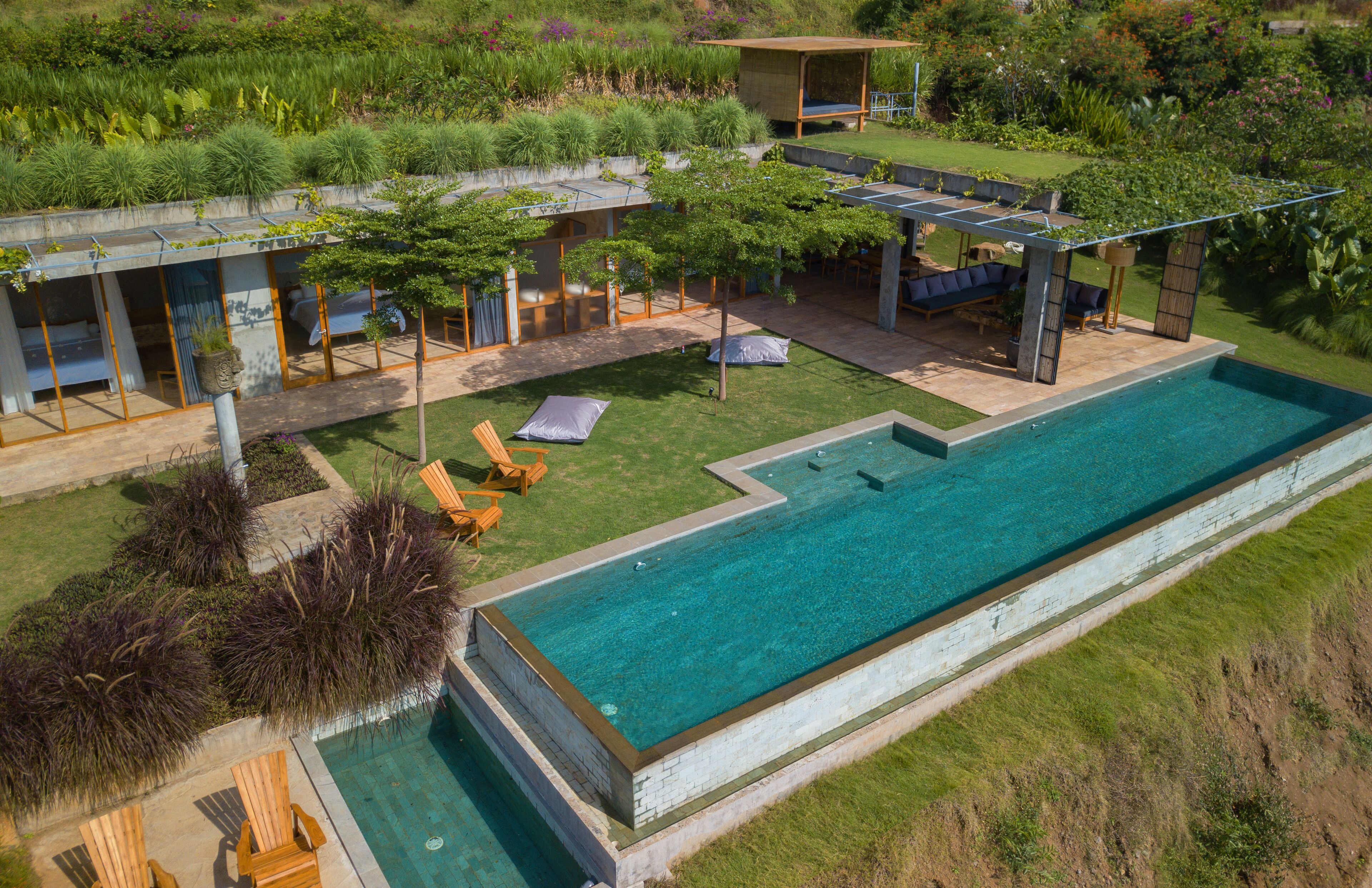 Uma área de piscina ao ar livre moderna, com espaço coberto para descanso e muita vegetação.