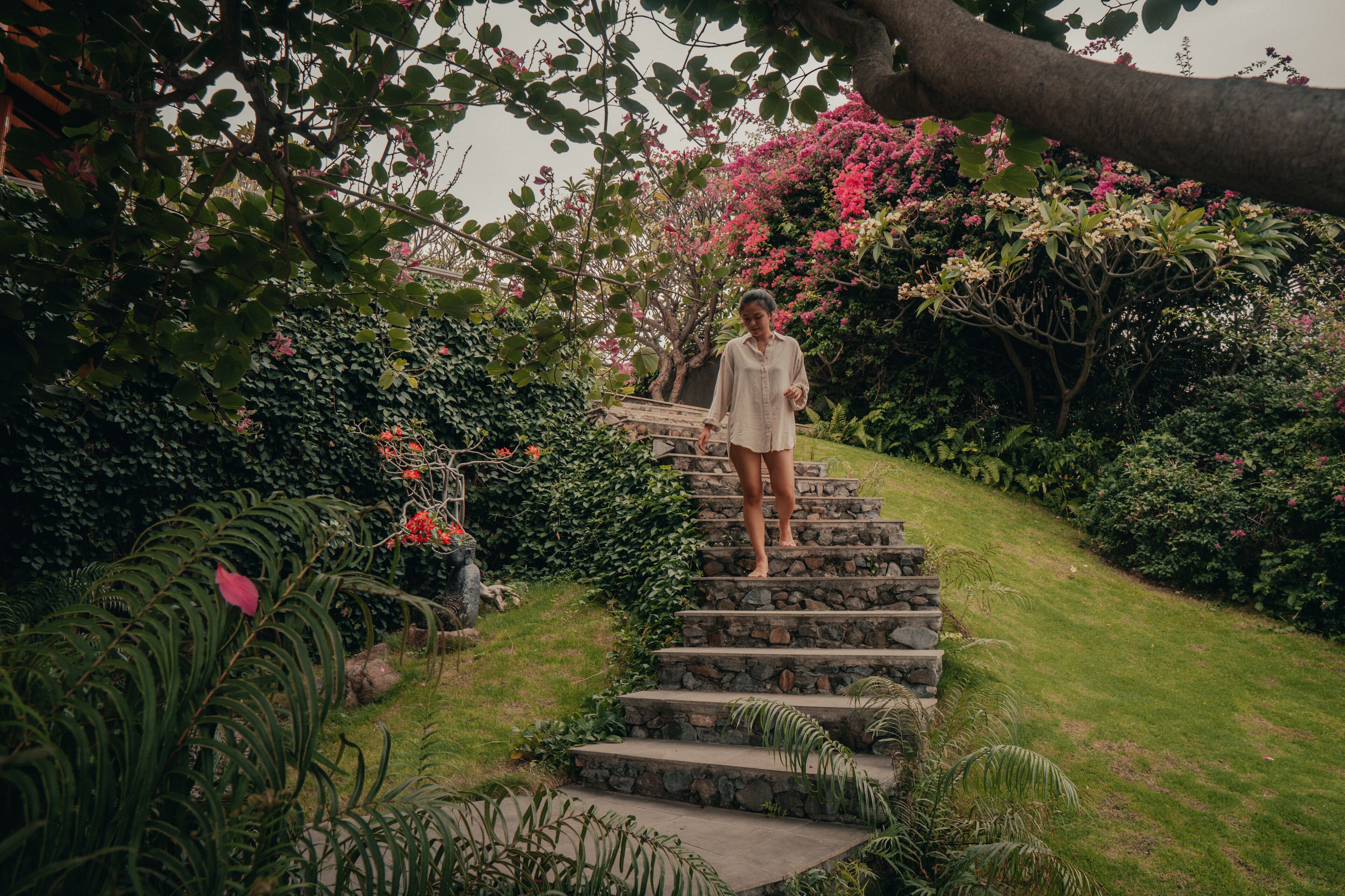 A person standing on stone steps surrounded by lush greenery and flowering plants.