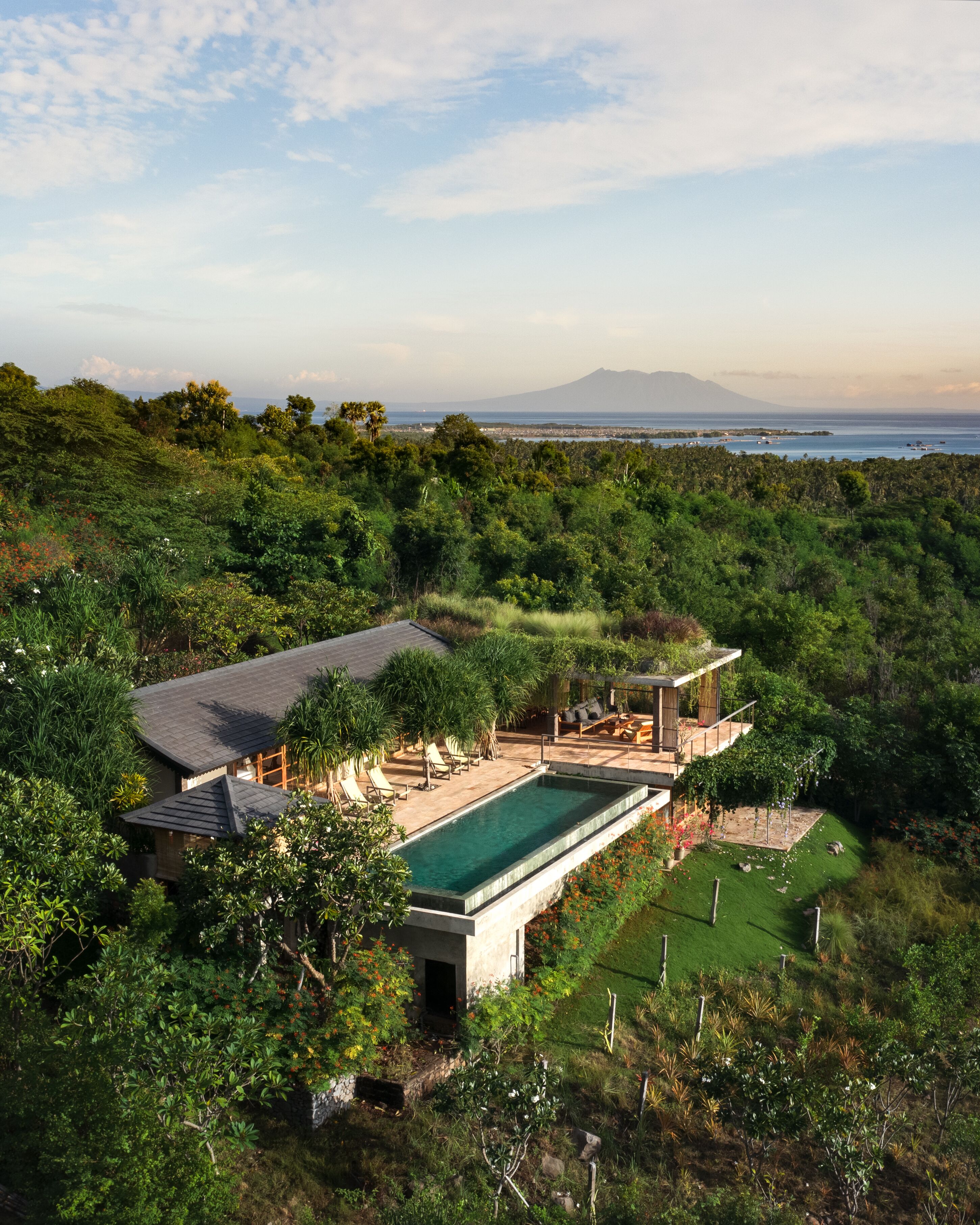 A modern house with a swimming pool, surrounded by lush greenery and a view of the ocean and a mountain.