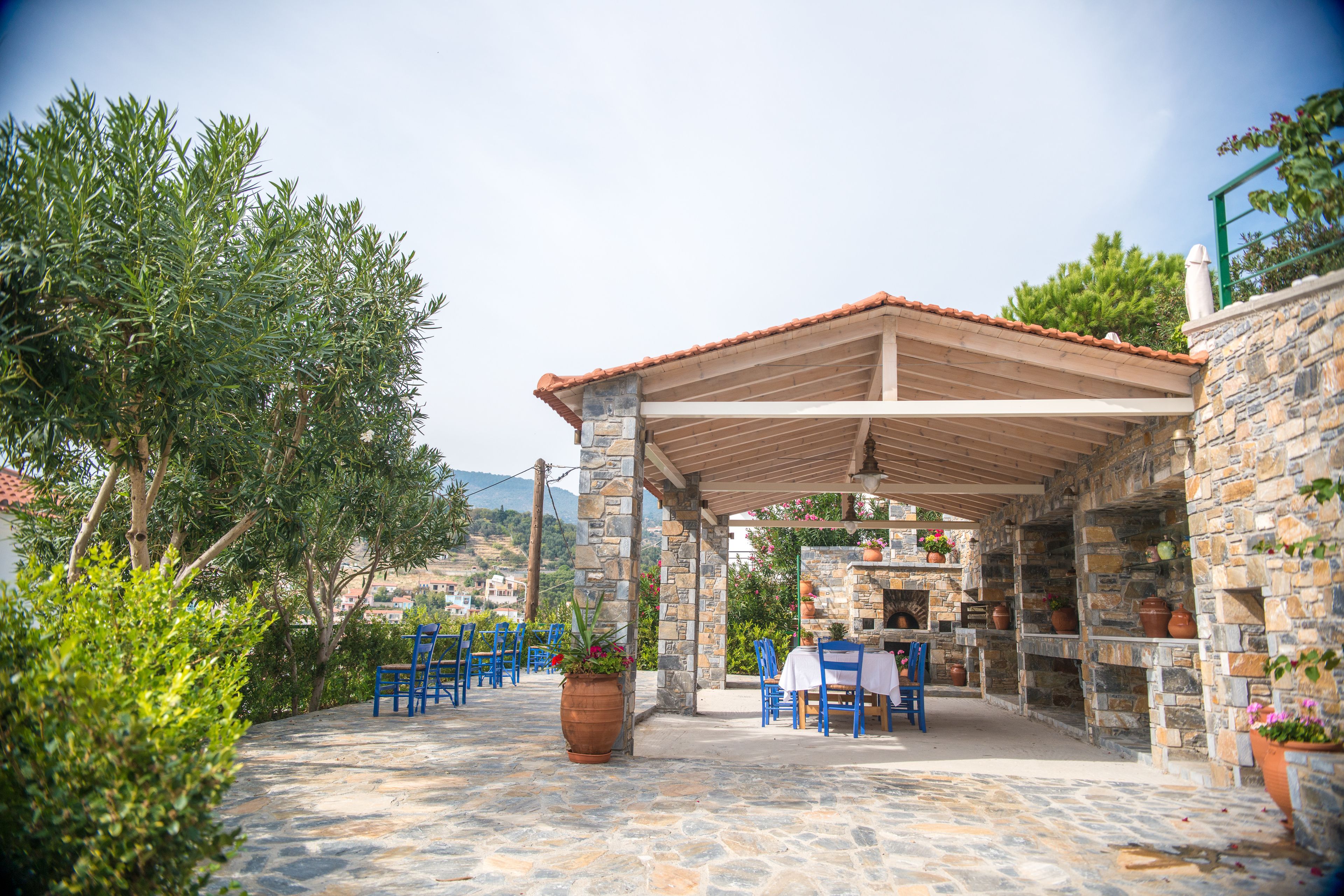 An outdoor patio with stone walls, blue chairs, and potted plants.