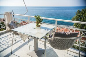 Una mesa de vidrio con mantel de encaje, una planta en maceta y sillas de mimbre en un balcón con vista al mar.
