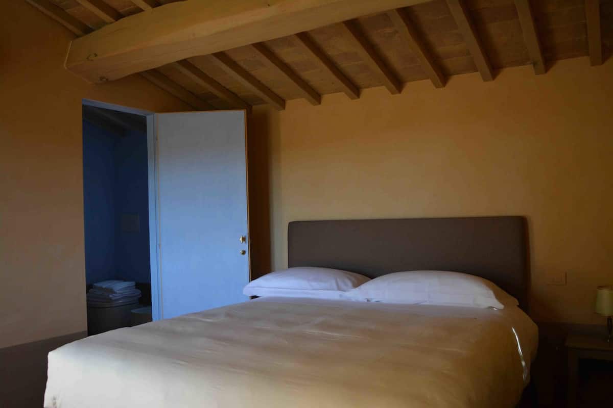 A bedroom with a bed, a door, and a nightstand with a lamp.