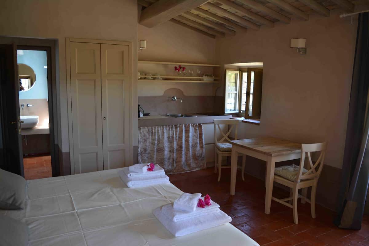 A bedroom with a bed, a desk, a chair, and a bathroom visible through an open door.