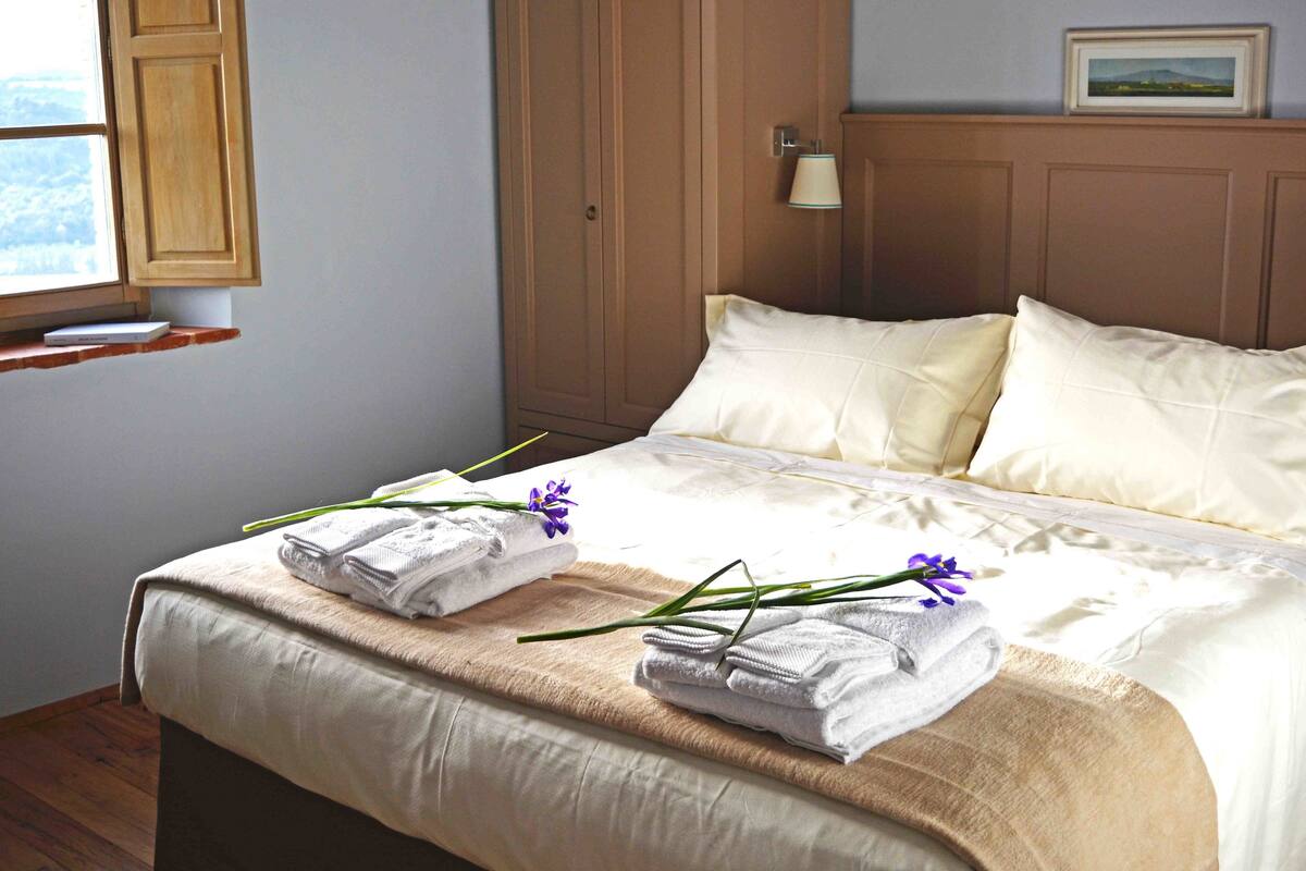 A neatly made bed with white linens and two folded towels on a beige bedspread.