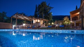 Una piscina con suelo de baldosas, una pérgola de madera y sillas de descanso.