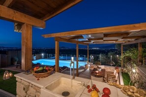 An outdoor kitchen area with a stone sink, a fruit basket, and a view of a swimming pool at night. - Villa Clairy (Zakynthos)