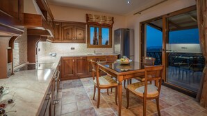 Una cocina moderna con armarios de madera, salpicadero de azulejos y una zona de comedor con mesa y sillas de vidrio.