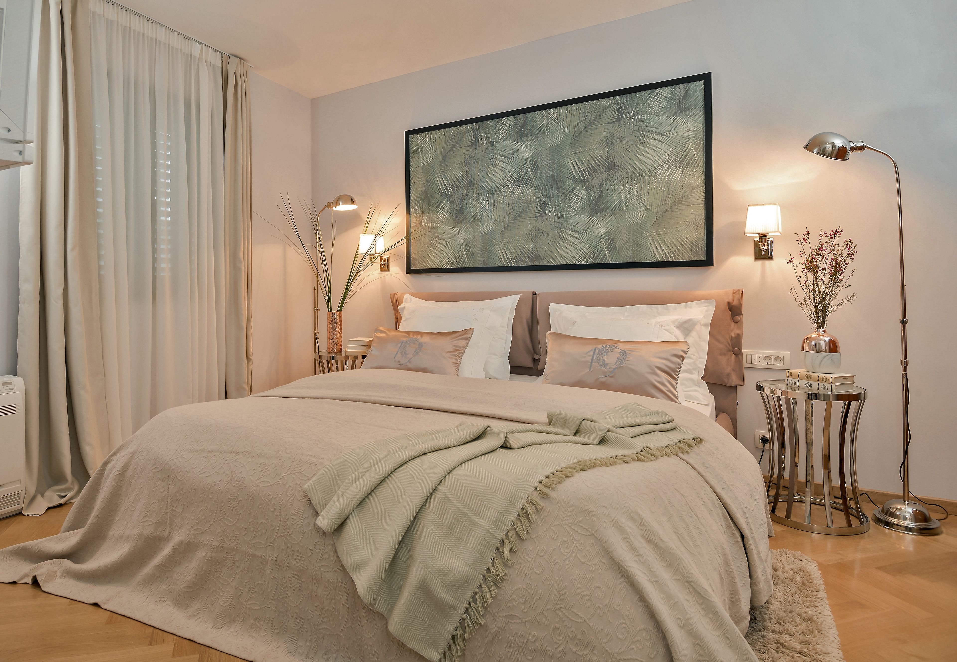A neatly made bed with a beige bedspread, two bedside lamps, and a framed artwork above the bed.