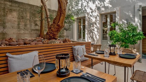 An outdoor dining area with wooden benches and tables, a tree, and a stone wall. - Heritage Hotel 19 (Split)