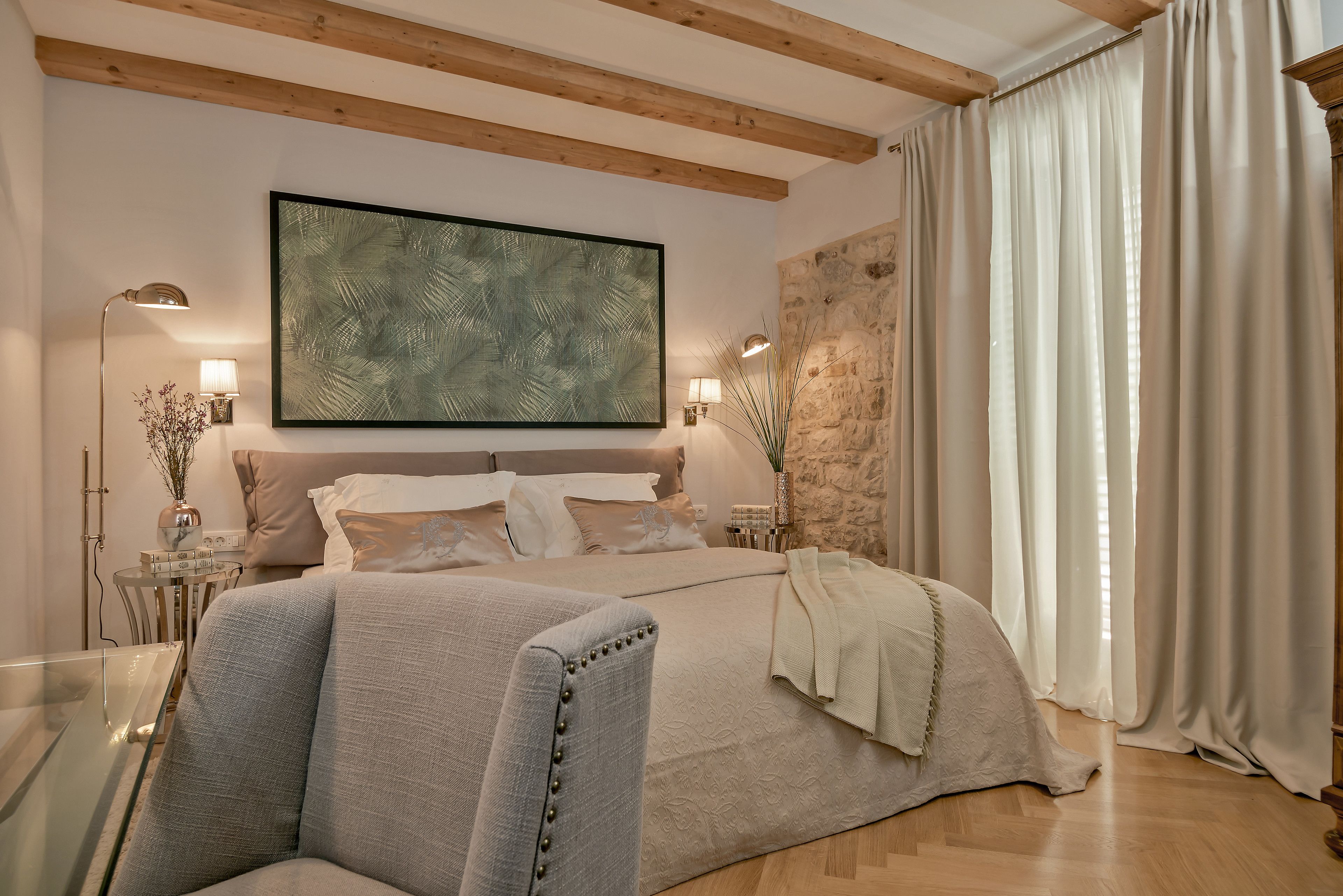 A modern bedroom with a large bed, a headboard with a stone accent, a large abstract painting, and a glass coffee table.