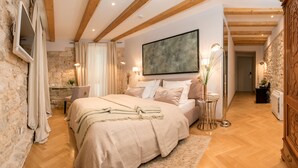 A bedroom with a large bed, a stone wall, wooden beams, a mounted artwork, and a bedside table with a lamp. - Heritage Hotel 19 (Split)