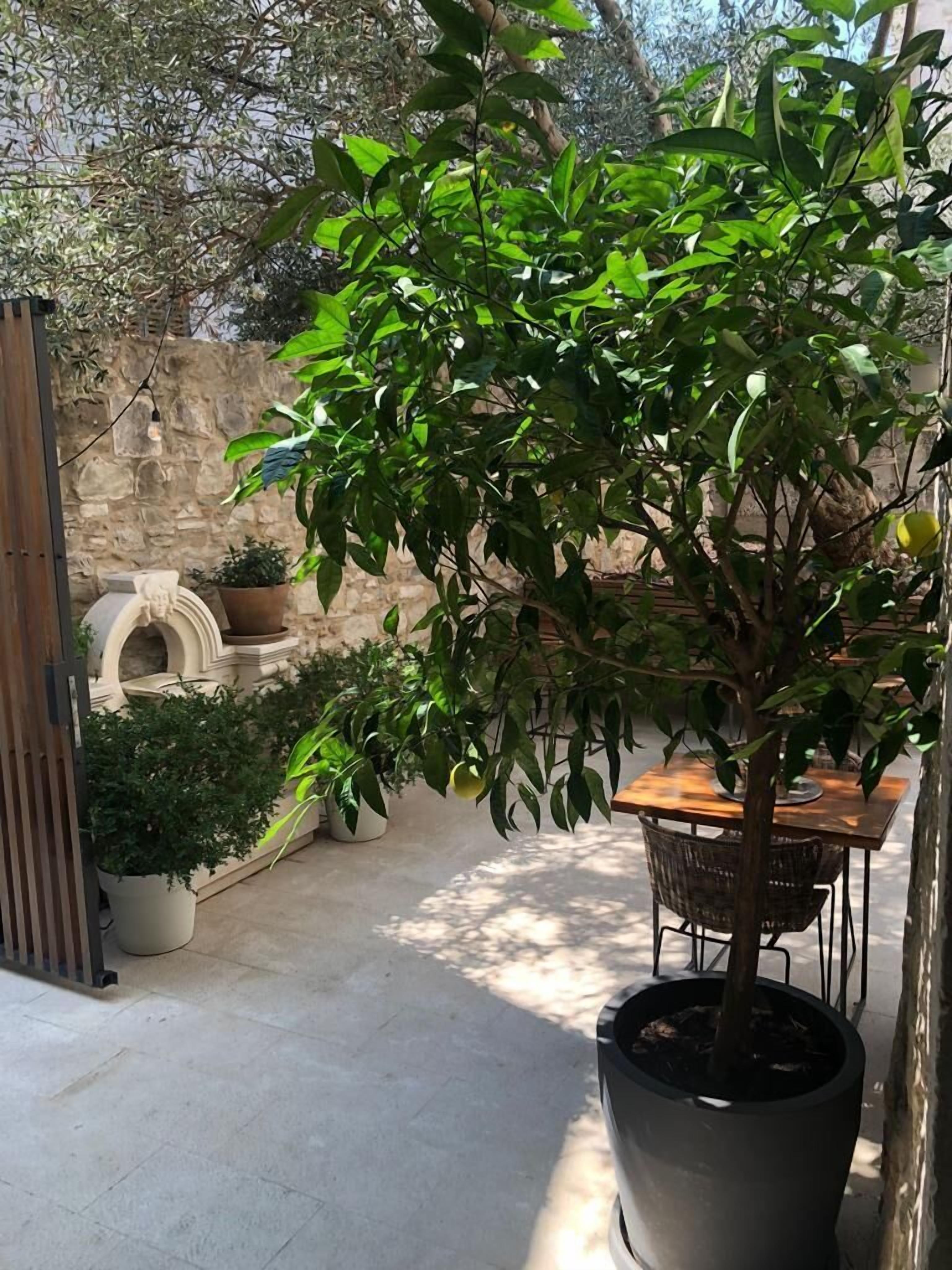 A patio area with a potted tree, a stone wall, and a table with chairs.