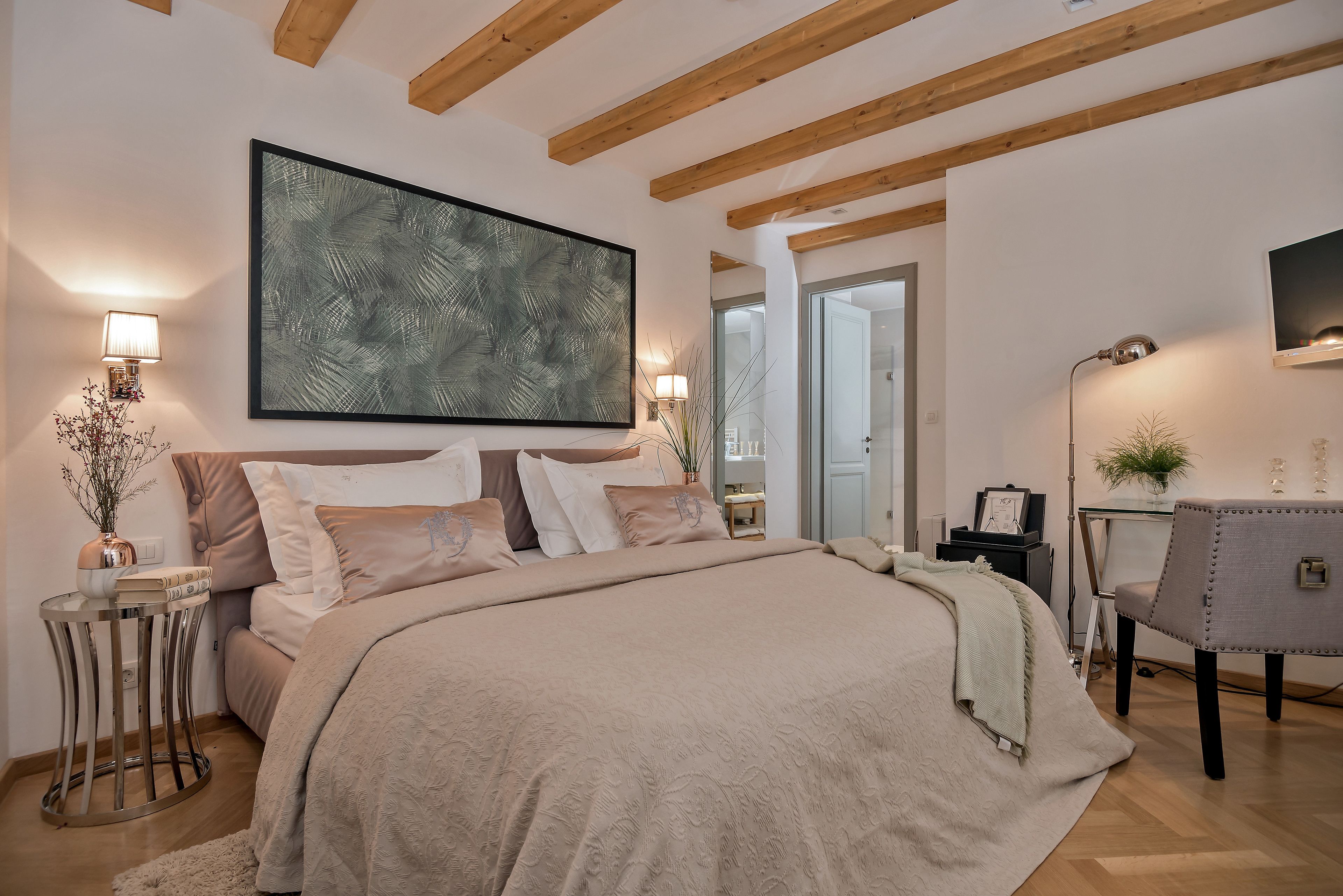 A bedroom with a large bed, a bedside table with a lamp, a wall-mounted TV, and a large abstract painting.