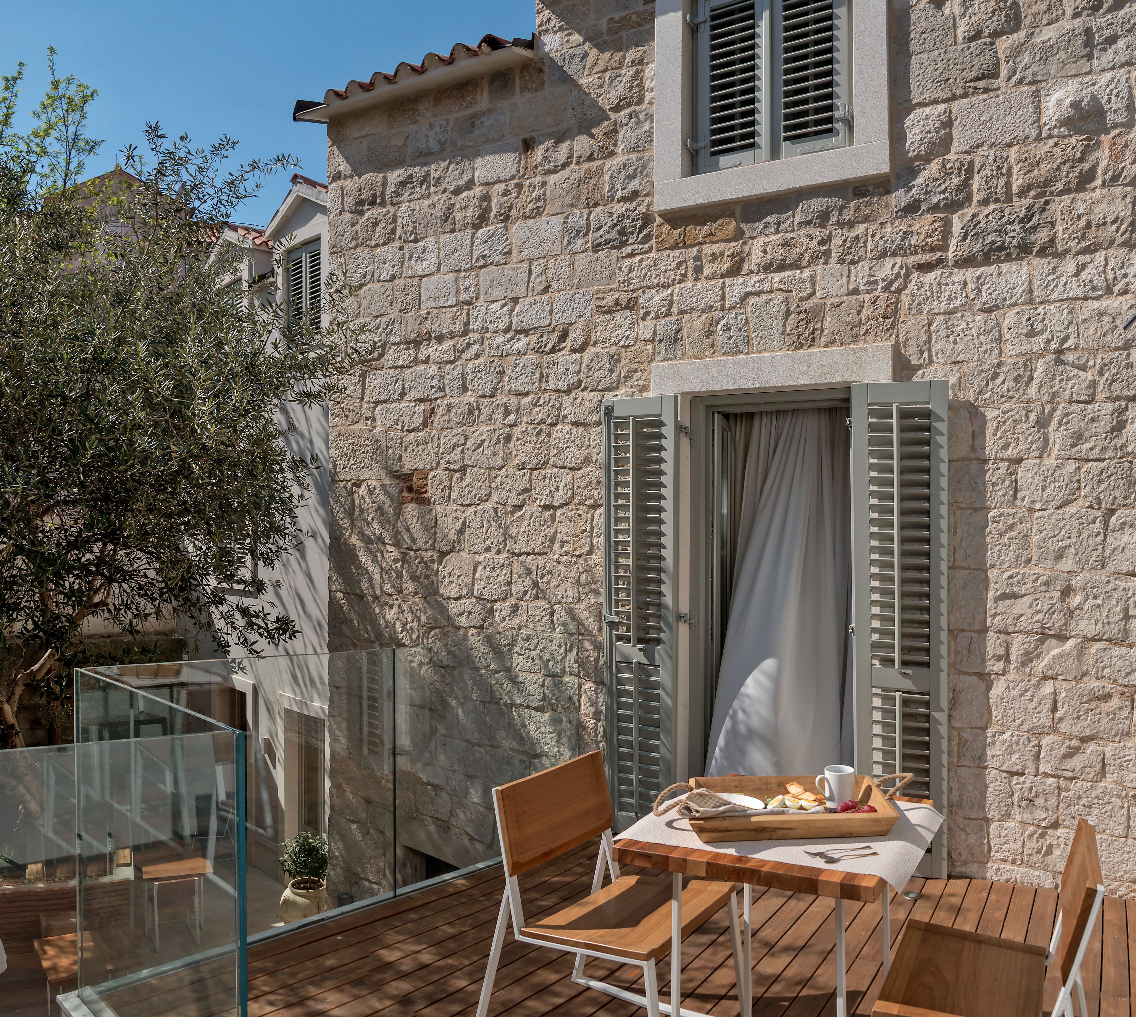 A stone building with a balcony, wooden furniture, and a table with food and a cup.