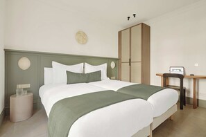 A double bed with a green throw, a wooden wardrobe, a small table with a laptop, and a round wall decoration.