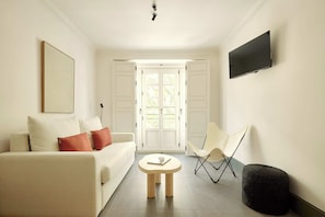 A modern living room with a sofa, a small round table, a chair, and a flat-screen TV mounted on the wall. - U-Sense Sevilla Santa Cruz (Seville)