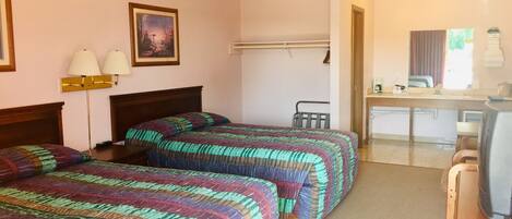 A hotel room with two beds, a desk, a chair, a small kitchenette, and a bathroom.