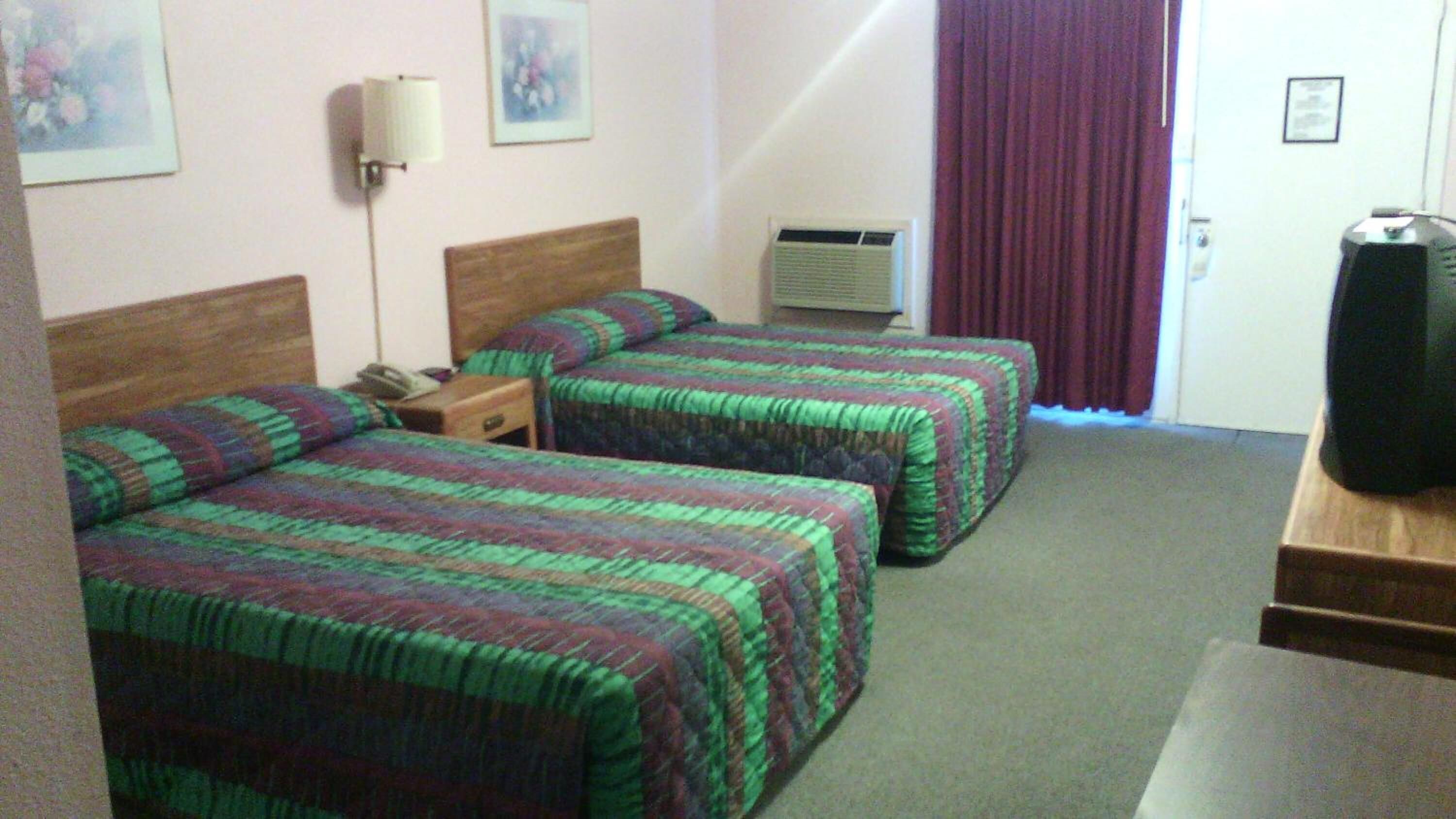 A hotel room with two beds, a desk, a lamp, an air conditioner, and a television.