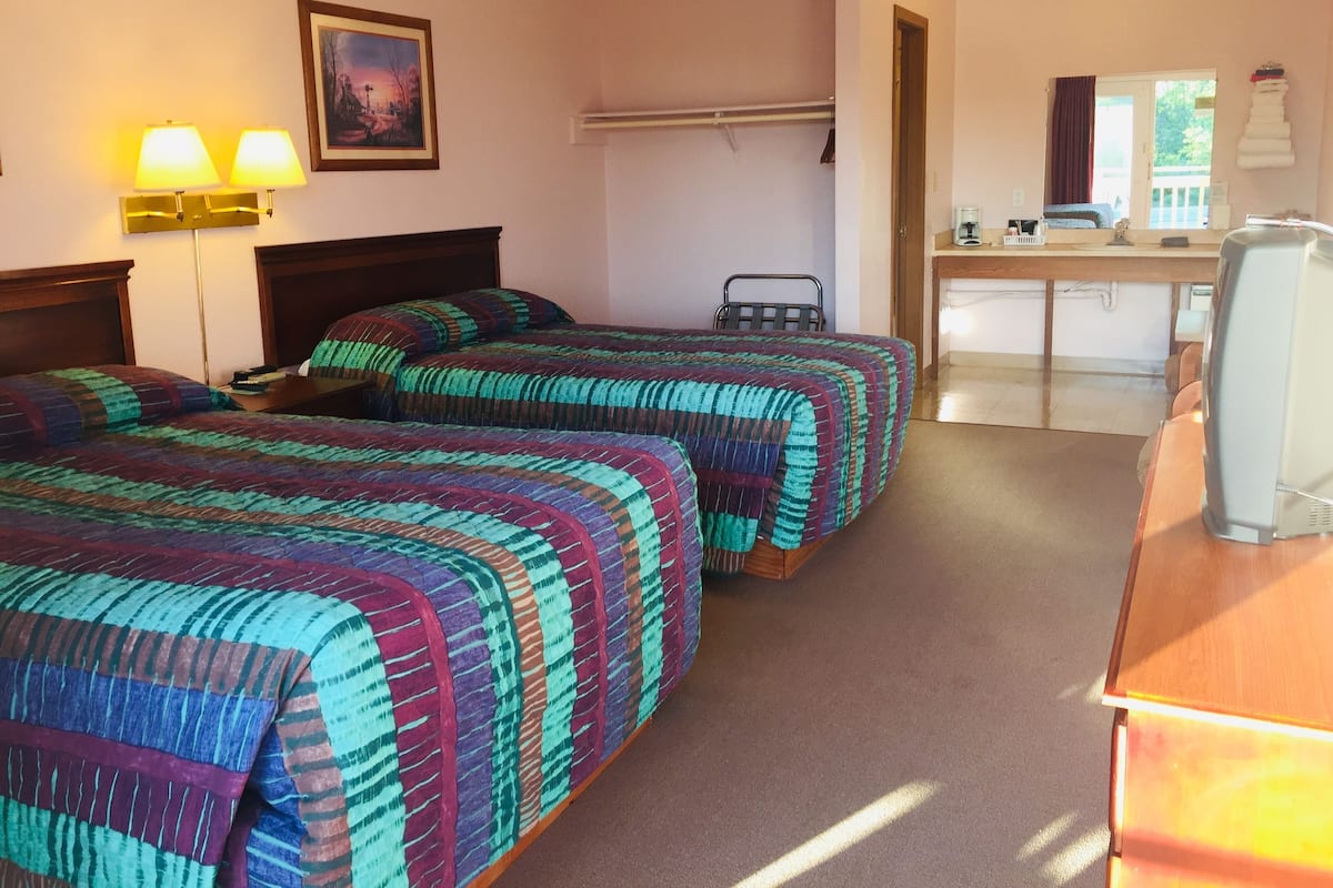 A hotel room with two beds, a desk, a chair, a lamp, and a painting on the wall.