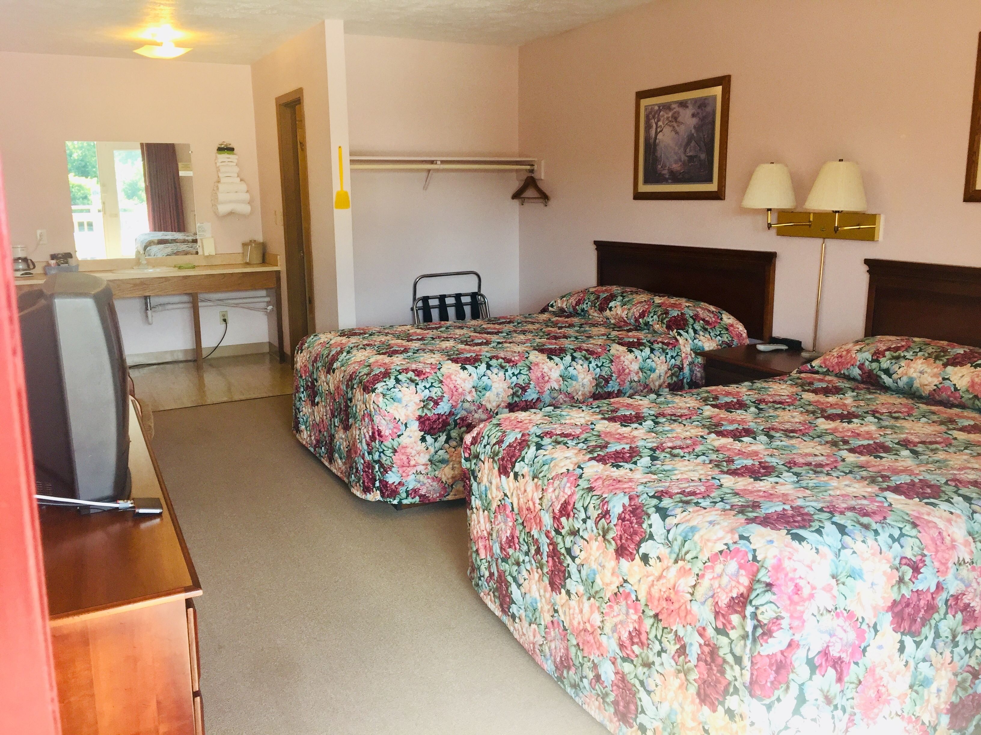 A hotel room with two beds, a desk, a chair, a lamp, and a painting on the wall.