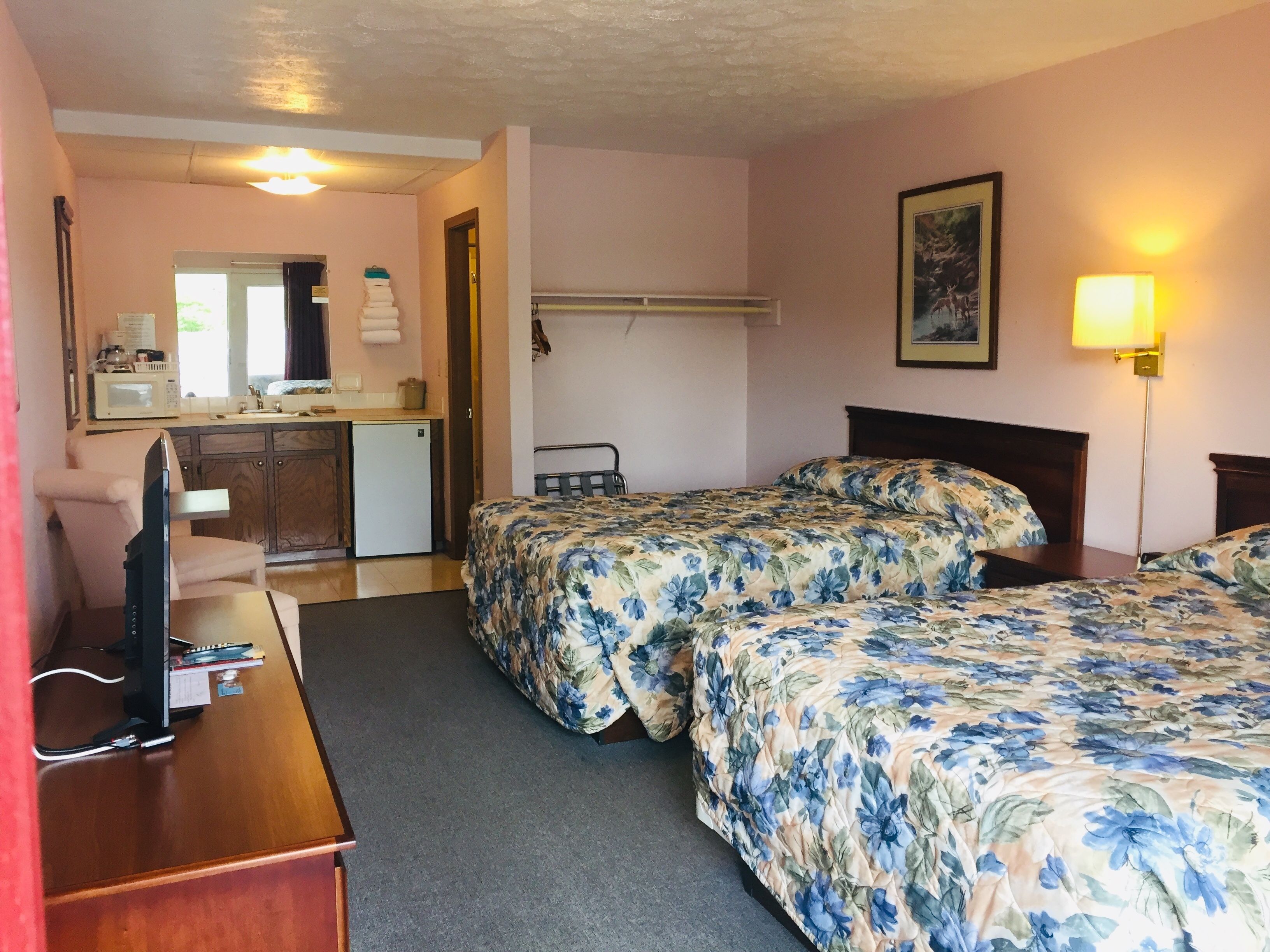 Habitació d'hotel amb llit, escriptori, cadira, microones i una cuineta petita.
