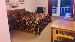 Une chambre d’hôtel équipée d’un lit, d’un bureau, d’une chaise, d’une télévision et d’un balcon donnant sur l’extérieur.