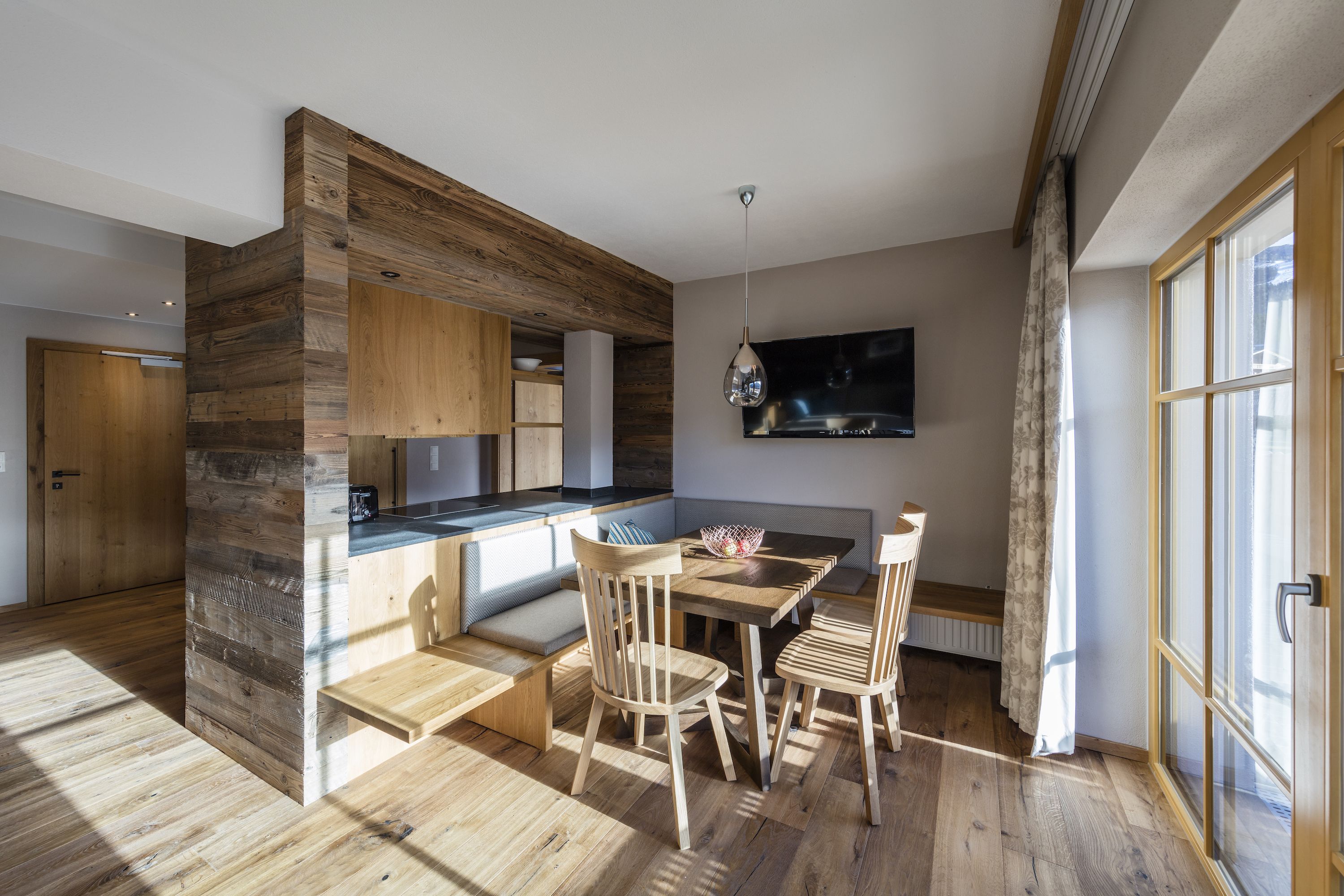 Una cucina moderna con elementi in legno, un'area pranzo con sedie di legno e un'ampia finestra con tende.