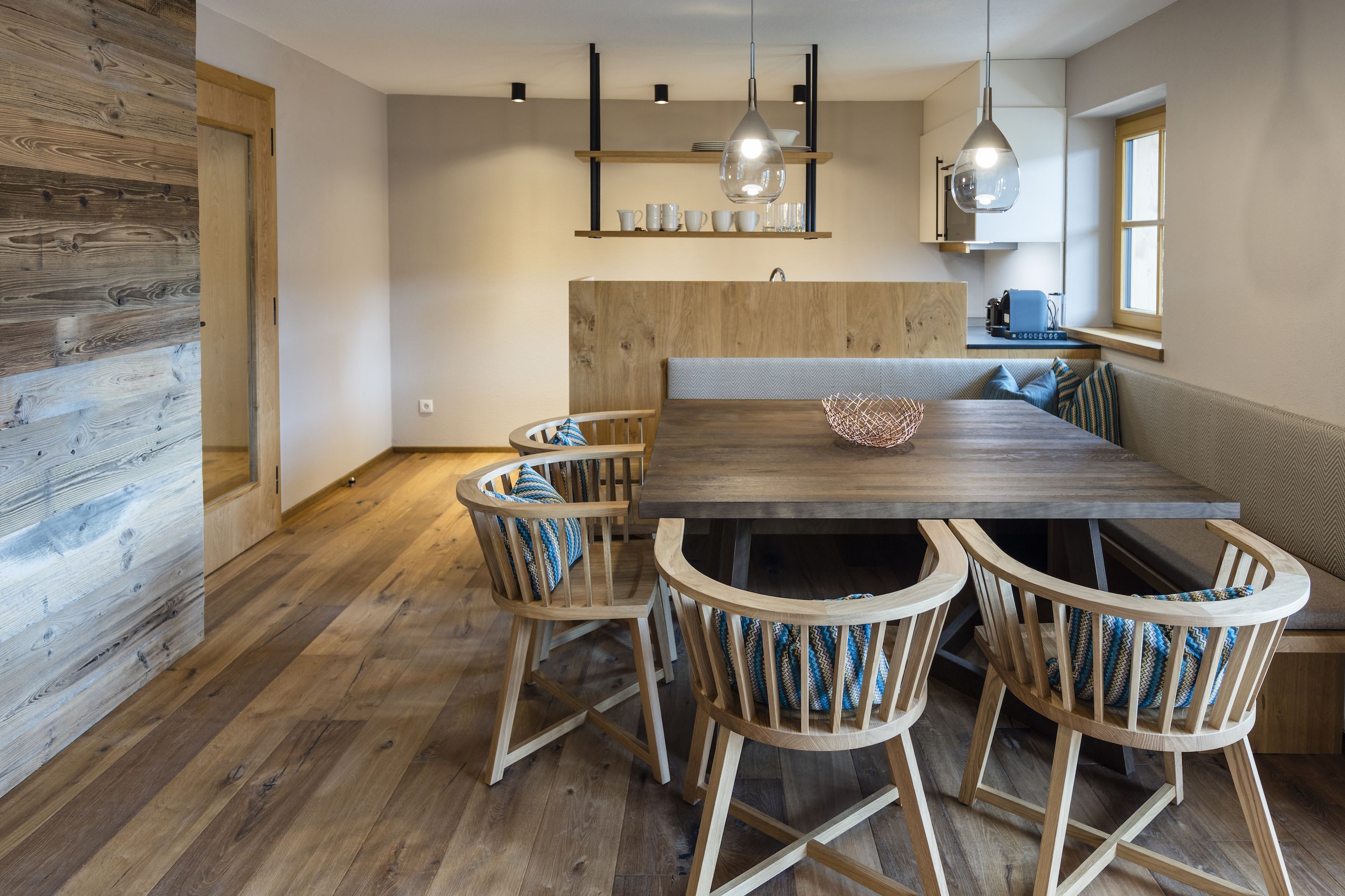 A modern kitchen with wooden cabinetry, a dining table with chairs, pendant lighting, and a window with a view.