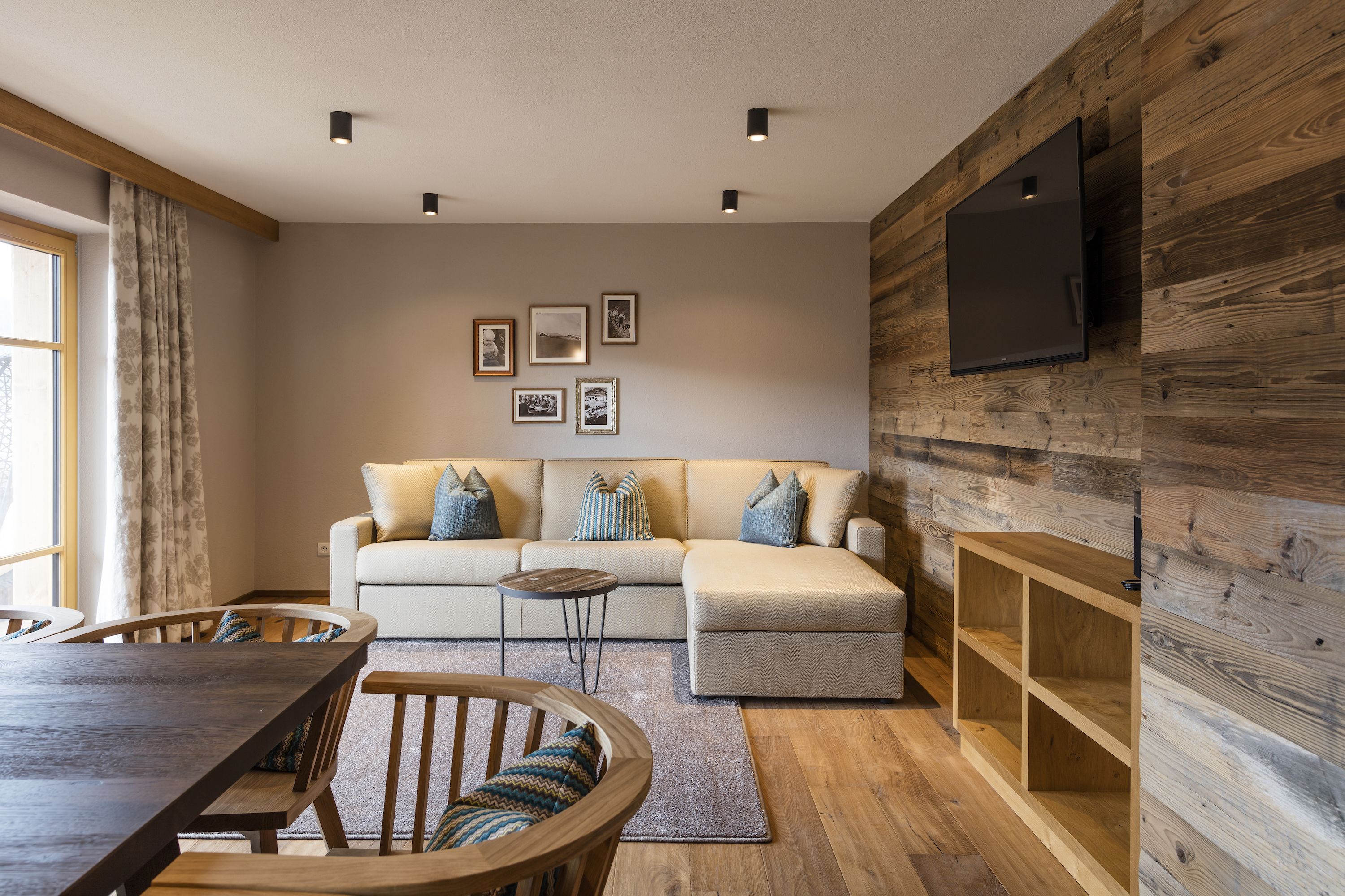 Una sala de estar moderna con un sofá, una mesa de comedor de madera y un televisor montado en una pared de madera.