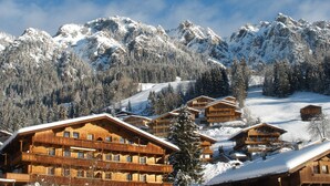 A wooden chalet-style hotel with multiple balconies and a view of snow-covered mountains. - Alpbach Lodge Chalet Superior (Alpbach)