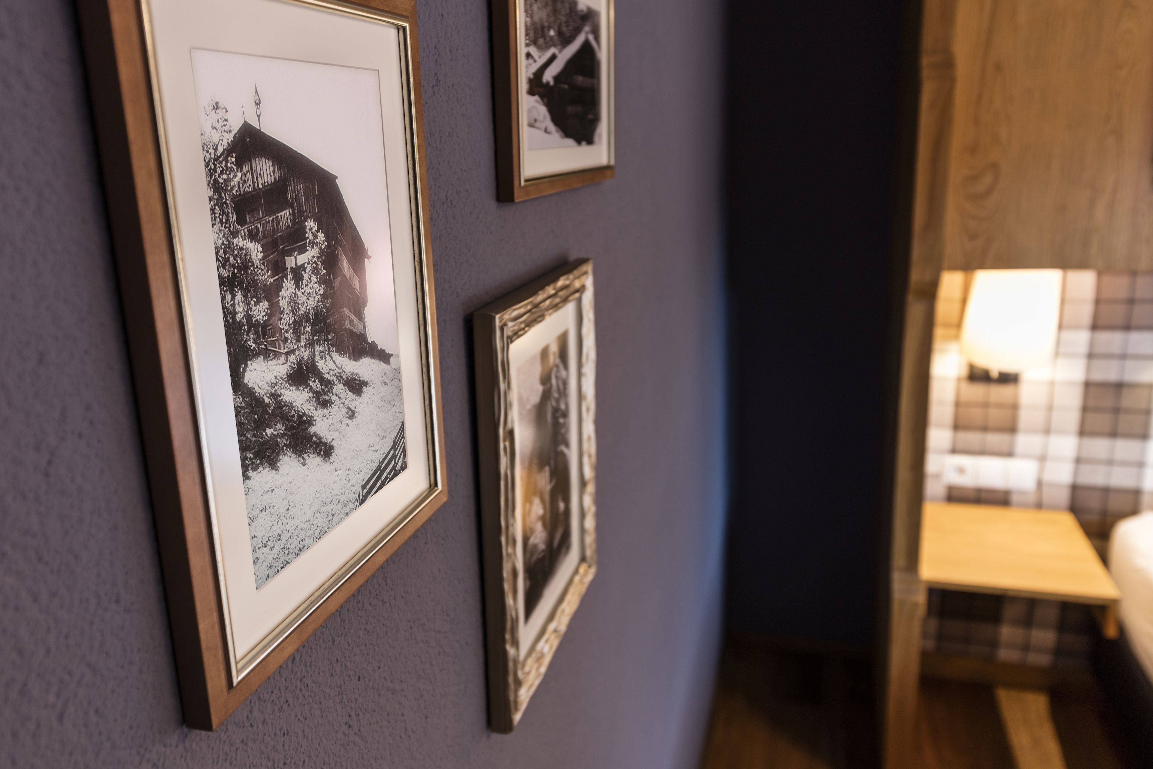 A wall with three framed photographs, a small wooden table, and a lamp.