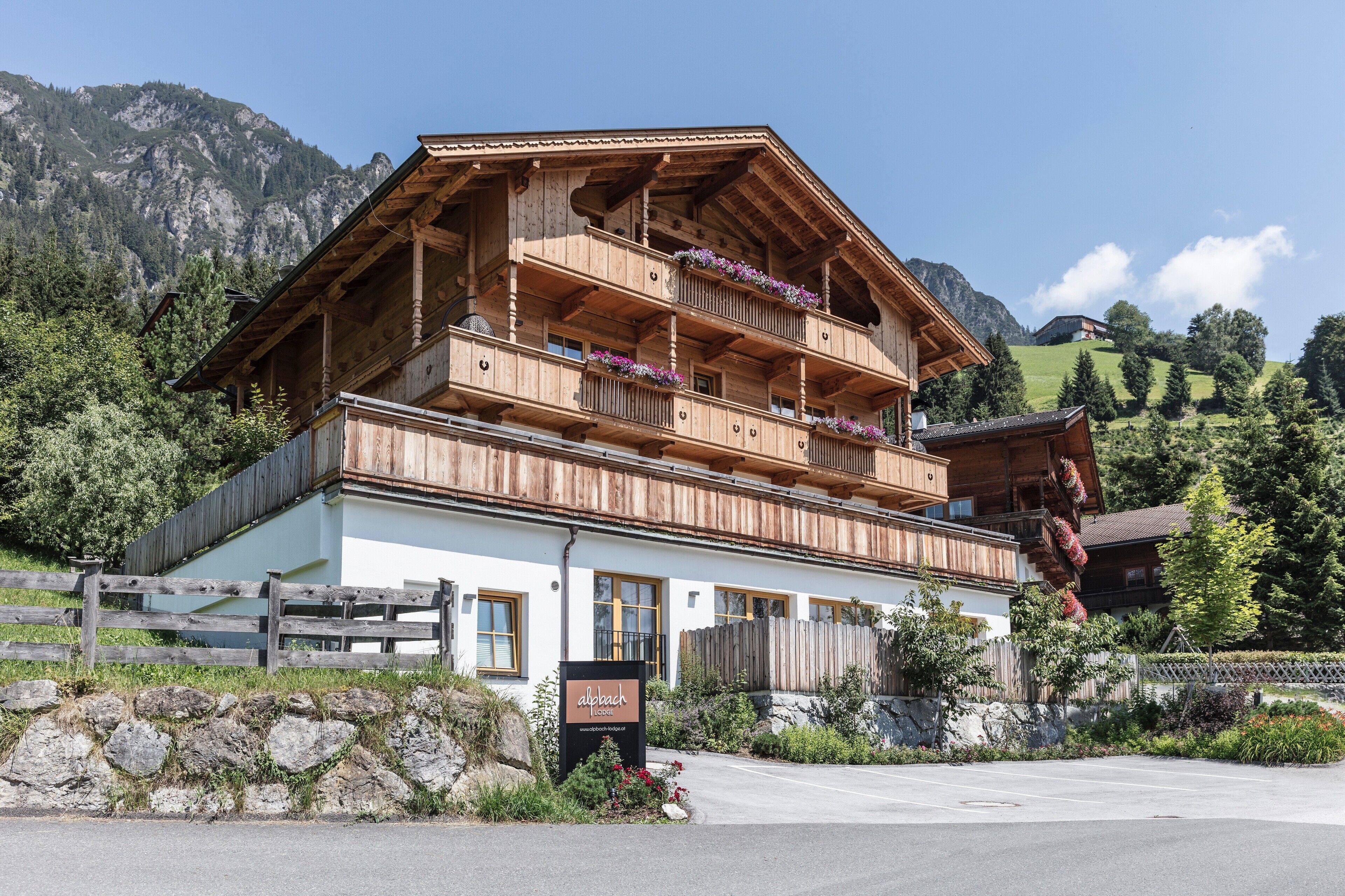 Una baita di legno con numerosi balconi, immersa nel verde e circondata da montagne.