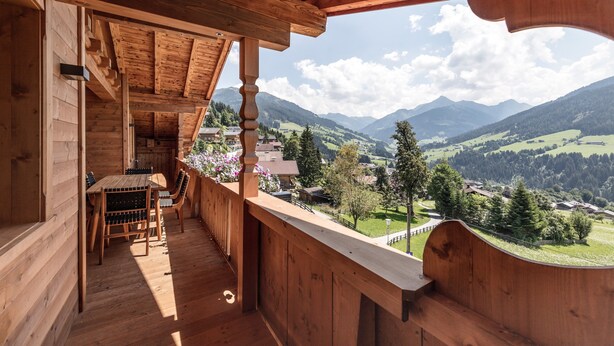 A wooden balcony with a table and chairs, overlooking a mountainous landscape. - Alpbach Lodge Chalet Superior (Alpbach)