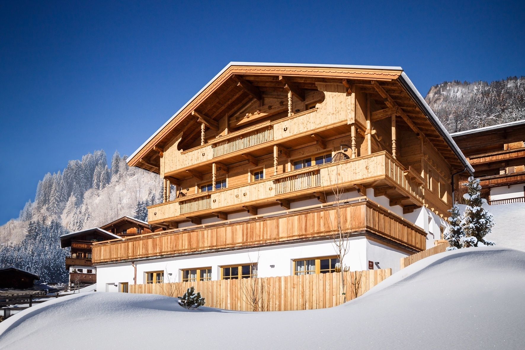 Una cabaña de madera de varios pisos con balcones, con una imponente montaña nevada de fondo.