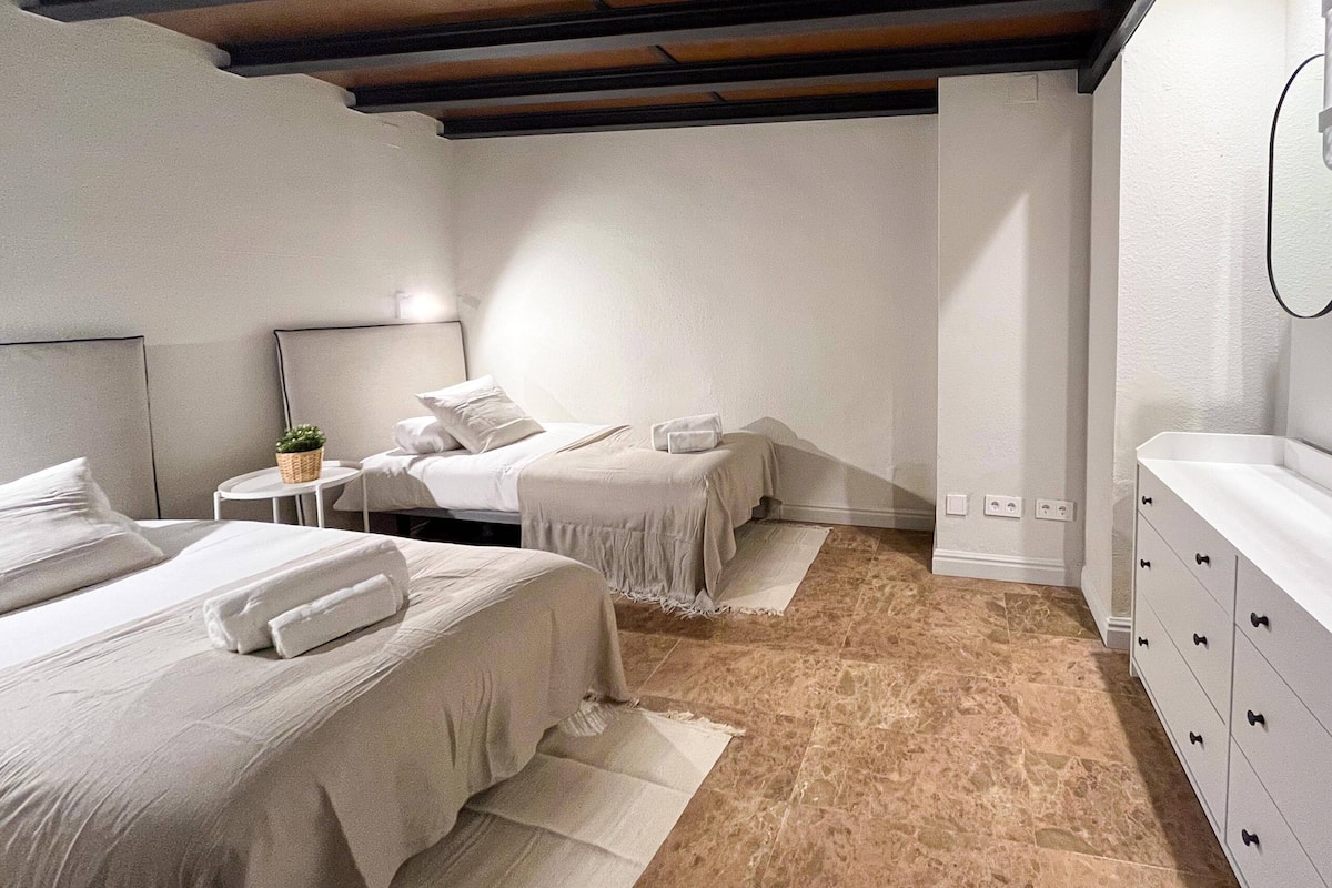 Un dormitorio con dos camas, una mesita de noche con lámpara, un aparador y una pequeña mesa con una planta.