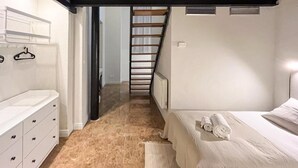 A bedroom with a bed, a nightstand, a dresser, and a staircase leading to another room. - VTZ Orús Factory Hotel - Parking Muy Económico (Zaragoza)