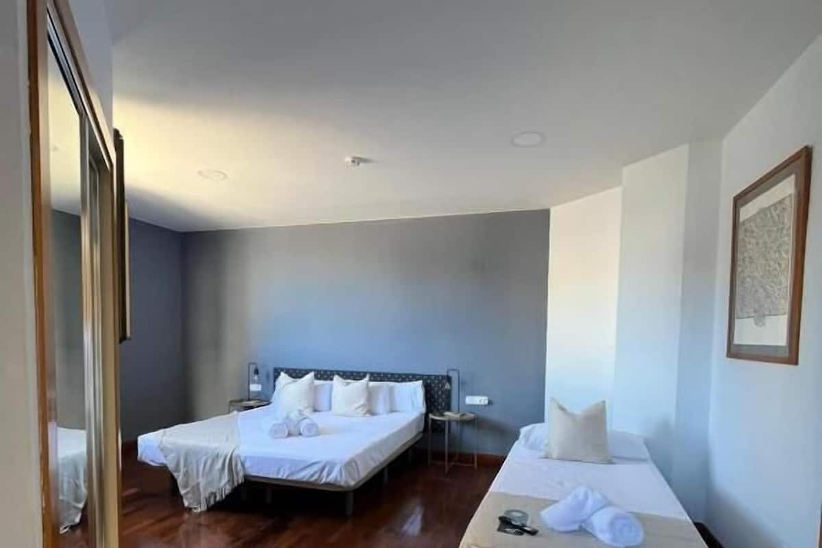 Habitación de hotel con dos camas, suelo de madera, un espejo grande y un cuadro enmarcado en la pared.