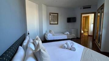 Une chambre d’hôtel avec deux lits, un téléviseur à écran plat, un tableau au mur et une porte donnant sur une autre pièce.