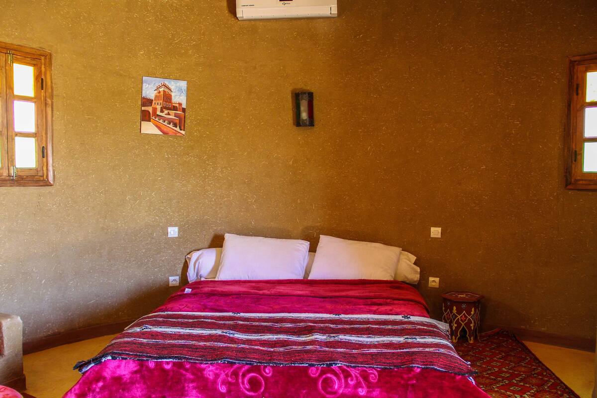 A room with a bed, a small table, a wall-mounted heater, and a window.