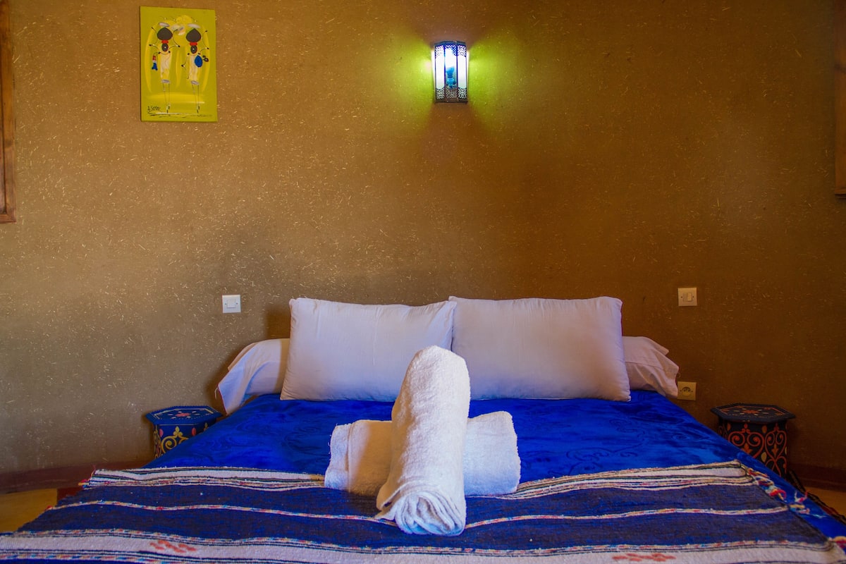 A neatly made bed with a blue and white striped bedspread, two white pillows, and a rolled white towel on the bed.