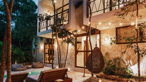 Un espacio lounge moderno al aire libre con piscina, mobiliario de madera e iluminación con luces colgantes.